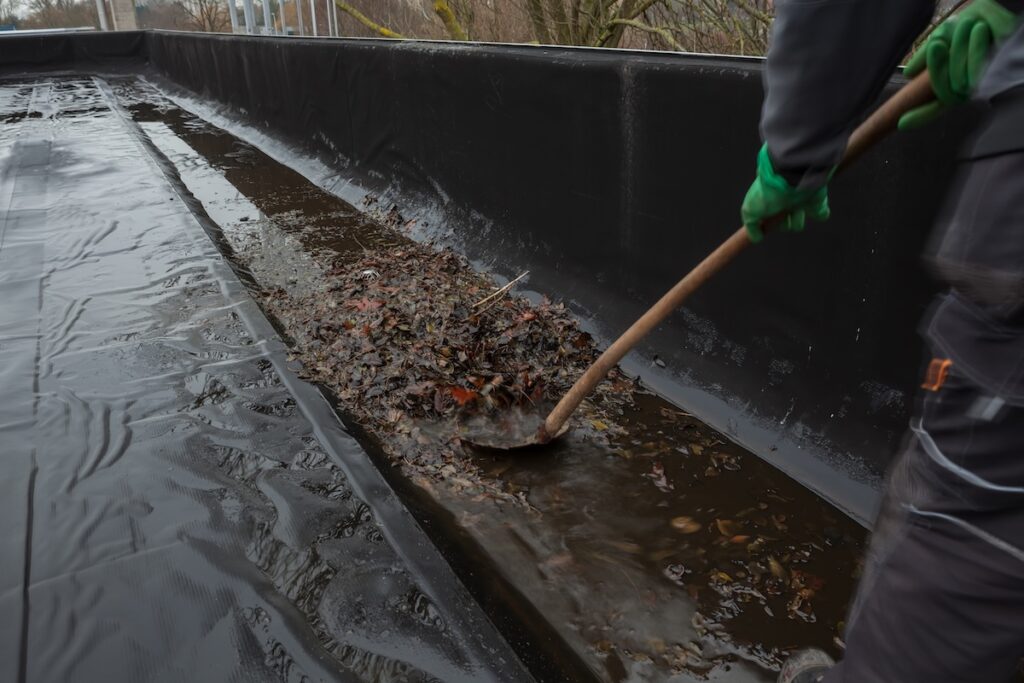The gutter of a flat roof is full of debris from the trees such as leaves and branches