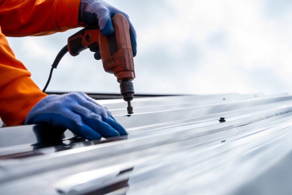 Roofer worker using air or pneumatic nail gun and installing metal sheet on top of the new roof.