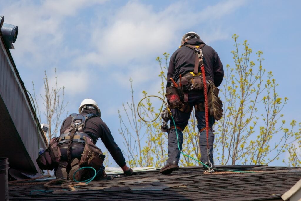 two roofers wearing extensive safety equipment while on house roof