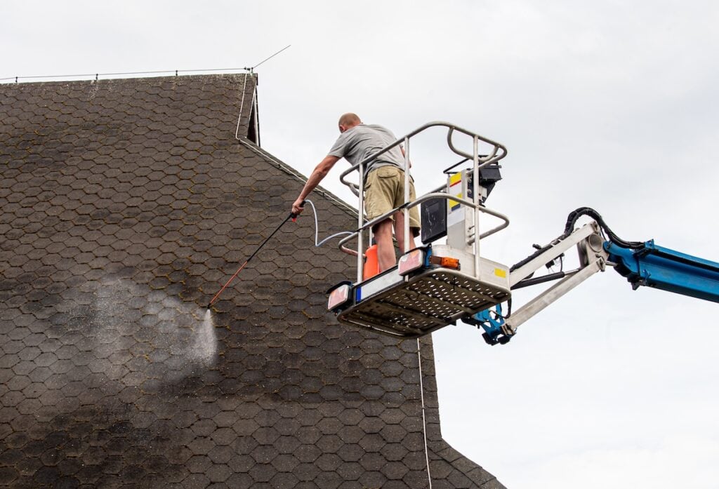 Man a homeowner spraying moss removing chemical to a domestic home roof