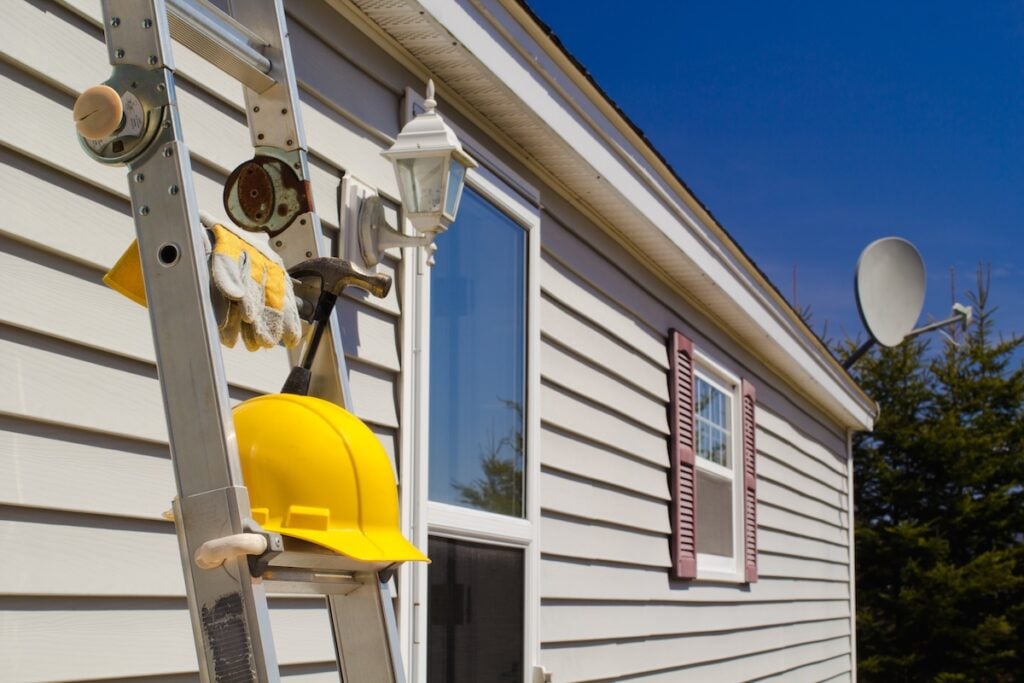 Yellow hard hat, work gloves and hammer on ladder with house in background