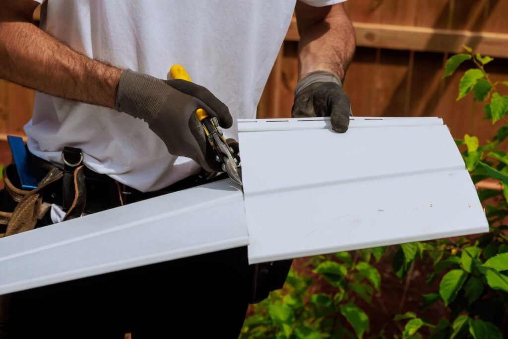 Worker cuts plastic vinyl siding to size before it is installed using scissors