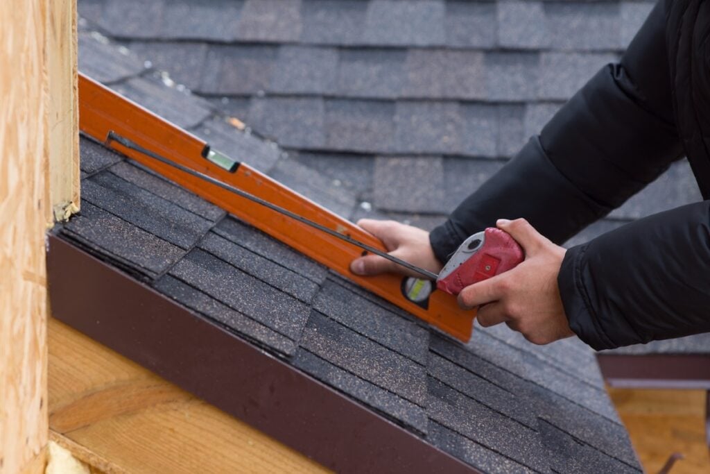 Roofer holding a tape measure and level on roof