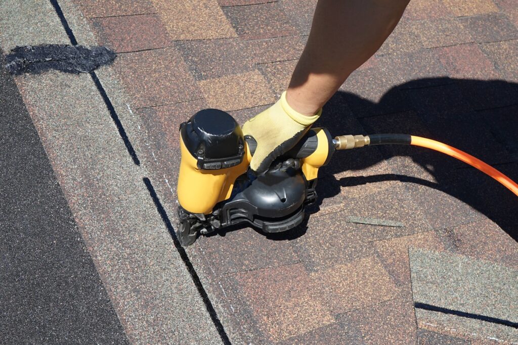 A roofer nailing shingles with air gun.