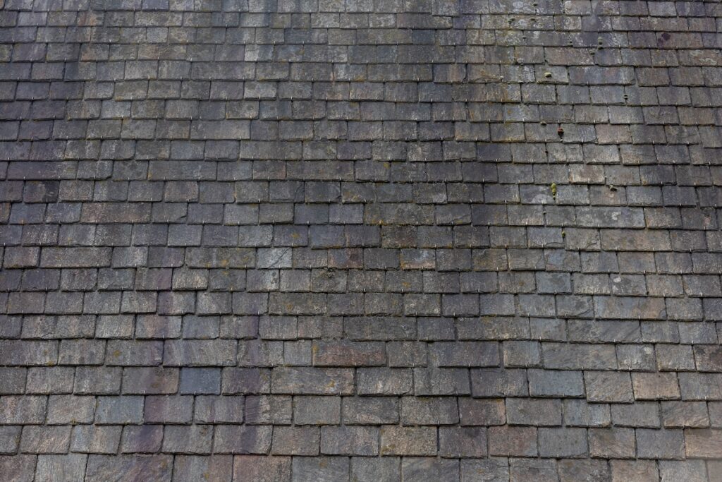 Old dark brown stone tiles covered with moss and rust stain on brick roof