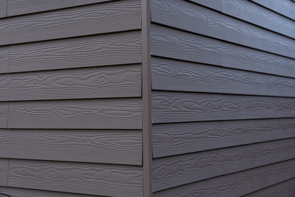 The corner of a house features gray horizontal siding with a wood grain texture, emphasizing clean lines 