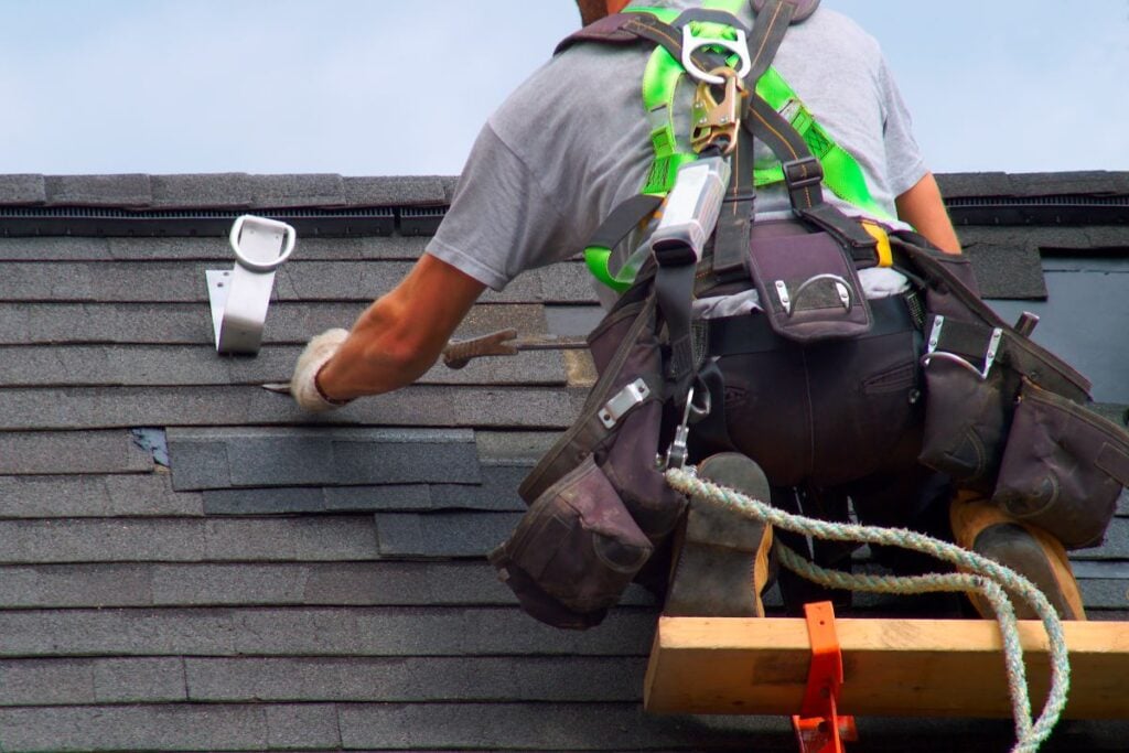 roofer repairing asphalt shingles after storm damage