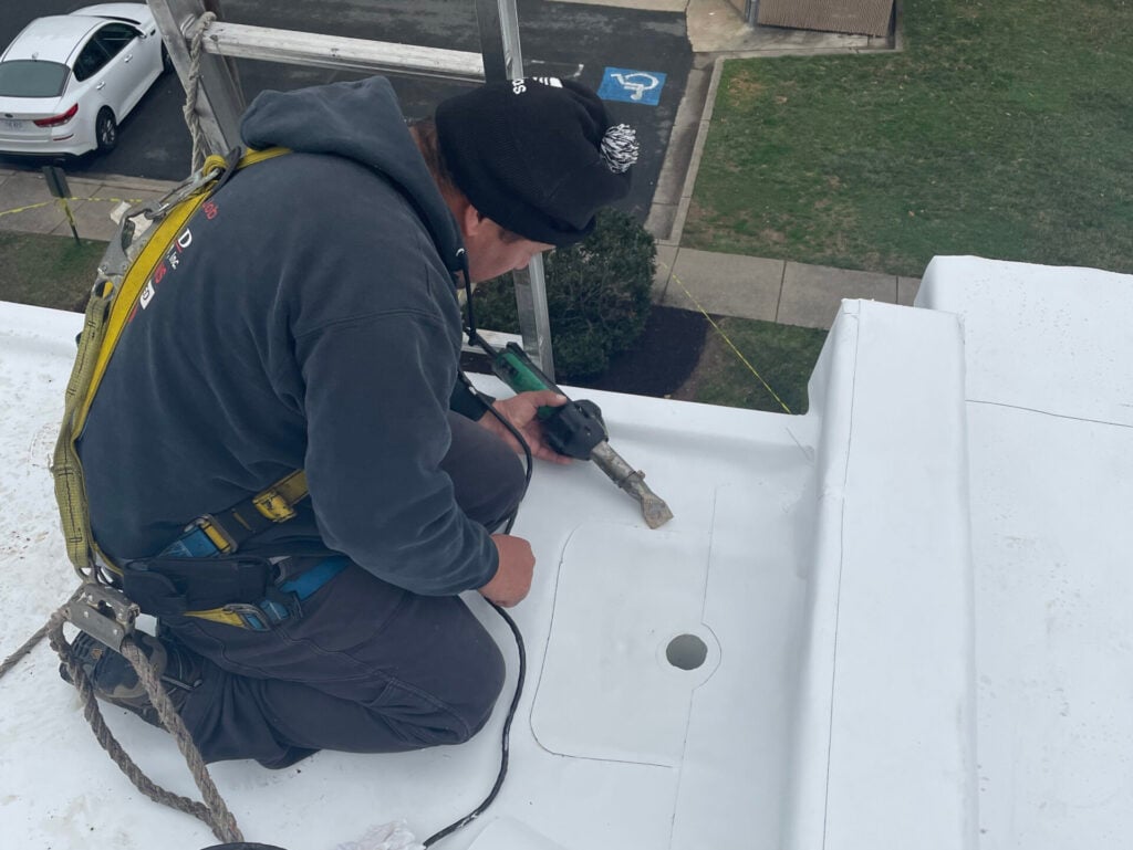 roofing maintenance programs worker using heating gun on TPO roof