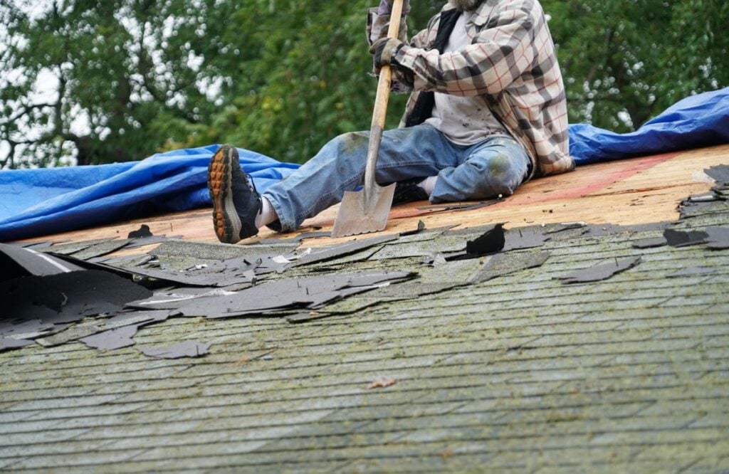 roof replacement process worker using shovel to remove shingles