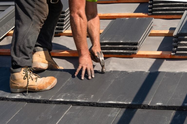 Worker driving nail into slate roof tile wearing steel-toe work boots