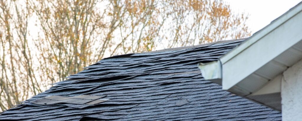 Asphalt shingles curled and lifted by strong wind along roof edge