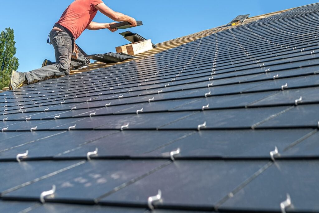 Roofer placing slate tiles on steep roof against blue sky