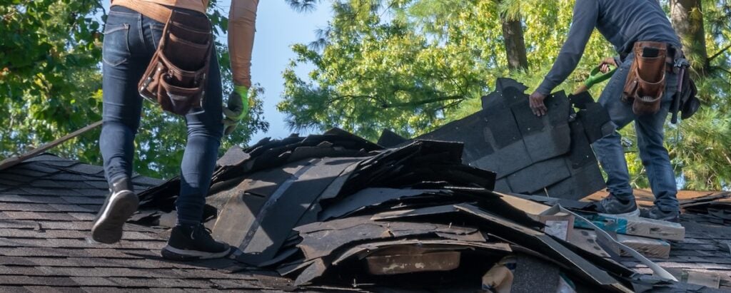 Roofing crew removing storm-damaged shingles from roof surface