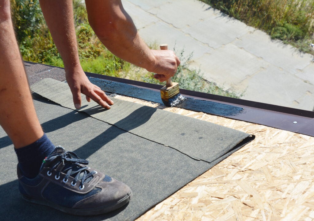 Worker applying sealant along metal flashing during shingle installation