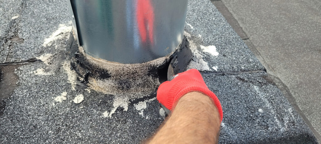 Worker resealing pipe boot flashing on asphalt shingle roof