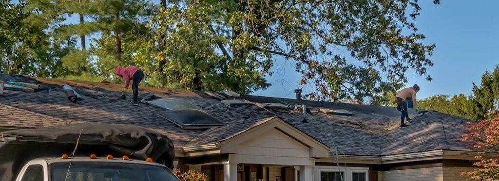 Two roofers repairing storm-damaged roof on a residential house