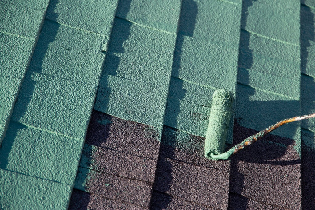 Roller applying green paint over asphalt shingle roof tiles