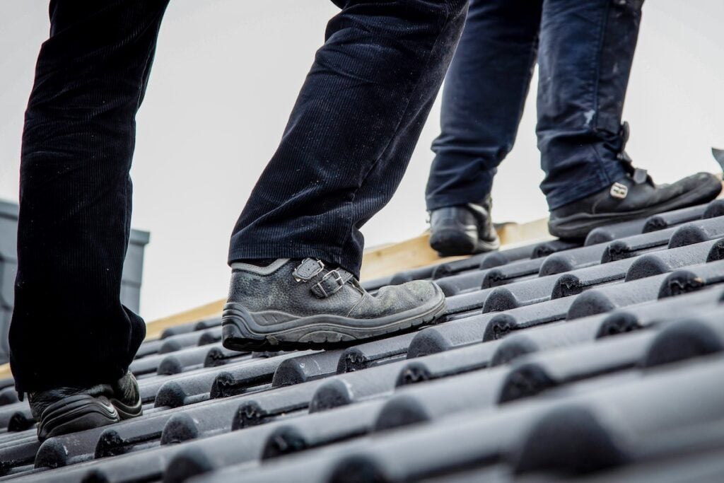 Two roofers walking across clay tile roof in traction work boots