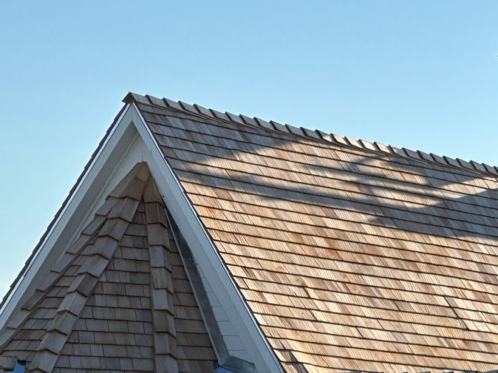 Cedar shake roof peak shows tapered shingle detail against blue sky