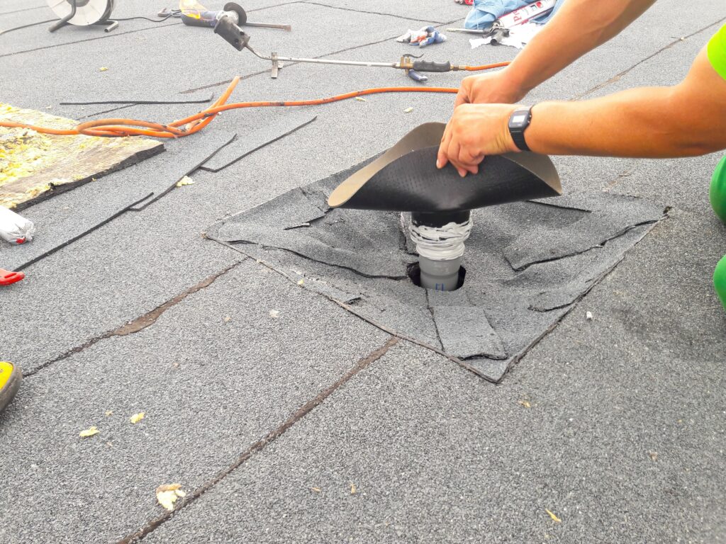 Worker installing a new rubber vent boot on a flat roof