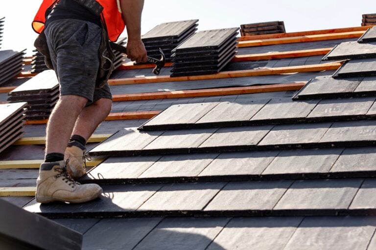 Contractor hammering slate tiles into place on roof deck