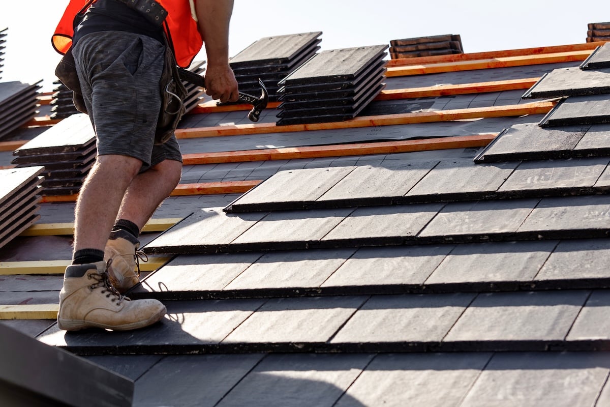 Contractor hammering slate tiles into place on roof deck