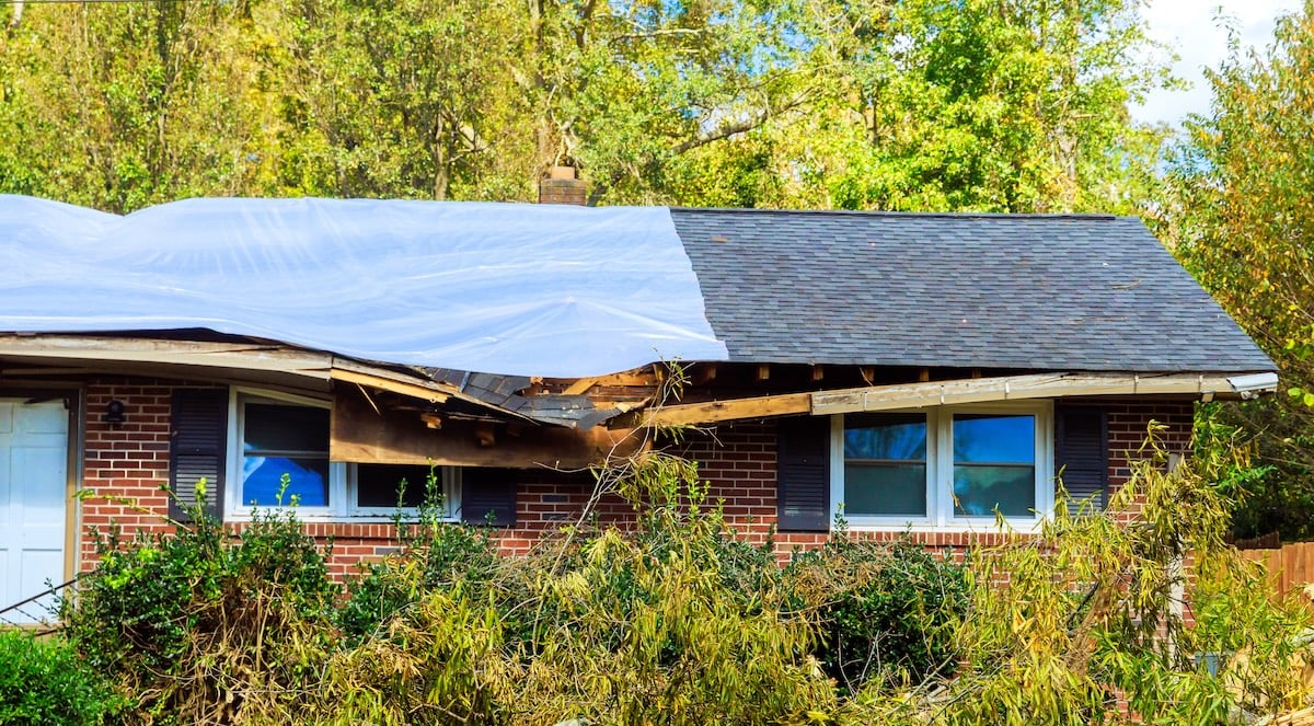 Blue tarp covering storm-damaged roof section on brick house