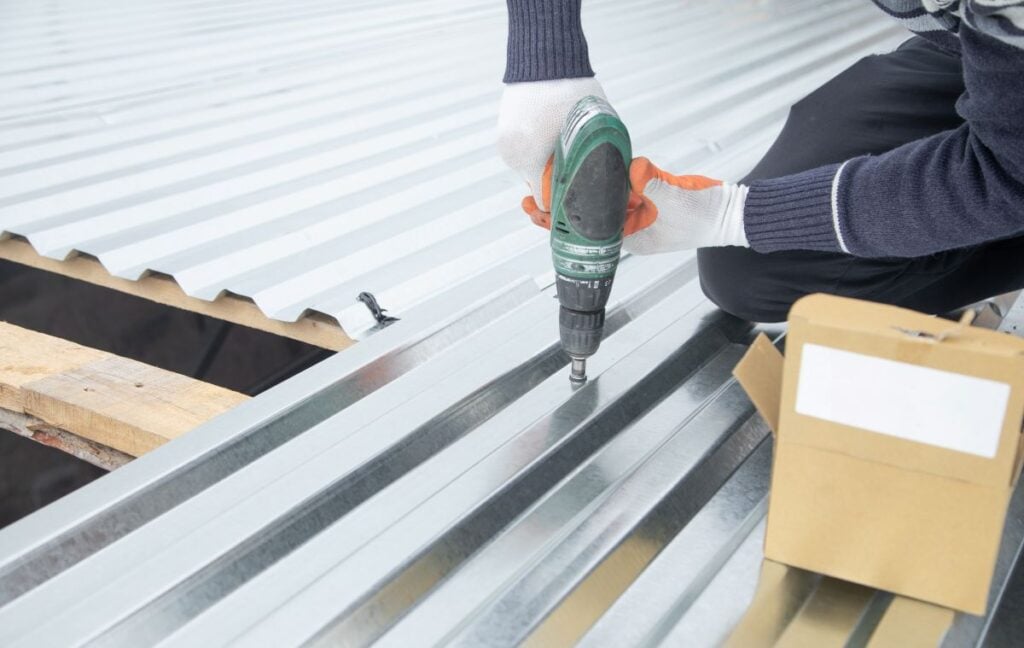 Man installing metal sheet roof by electrical drilling machine
