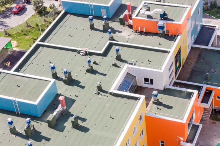 Top view flat roof with air conditioners and hydro insulation membranes on top of a modern blue and orange apartment building