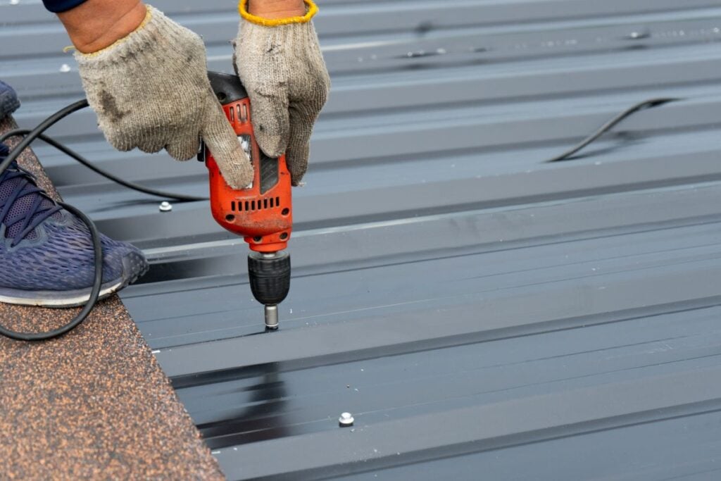 Workers installing the metal sheet roof by electrical drilling machine