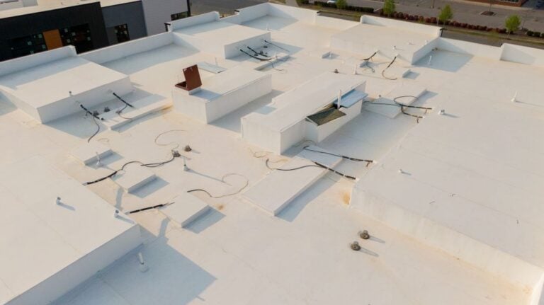 Aerial drone inspection of commercial TPO roof featuring heat-welded seams, HVAC curb flashing, and pipe penetrations