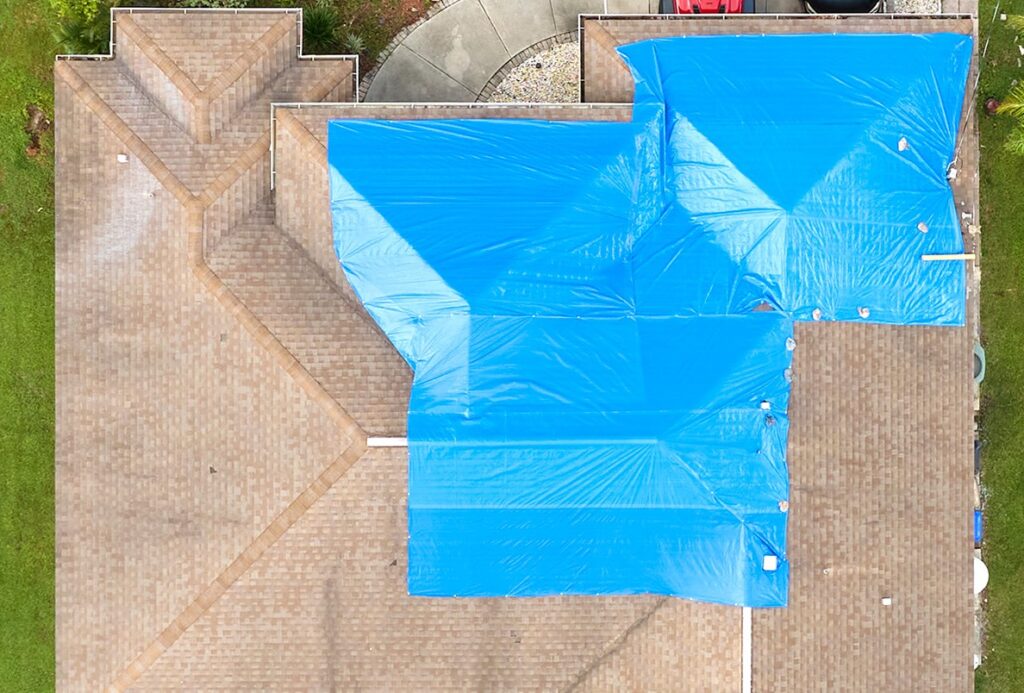 Top view of leaking house roof covered with protective tarp sheets against rain water leaks until replacement of asphalt shingles
