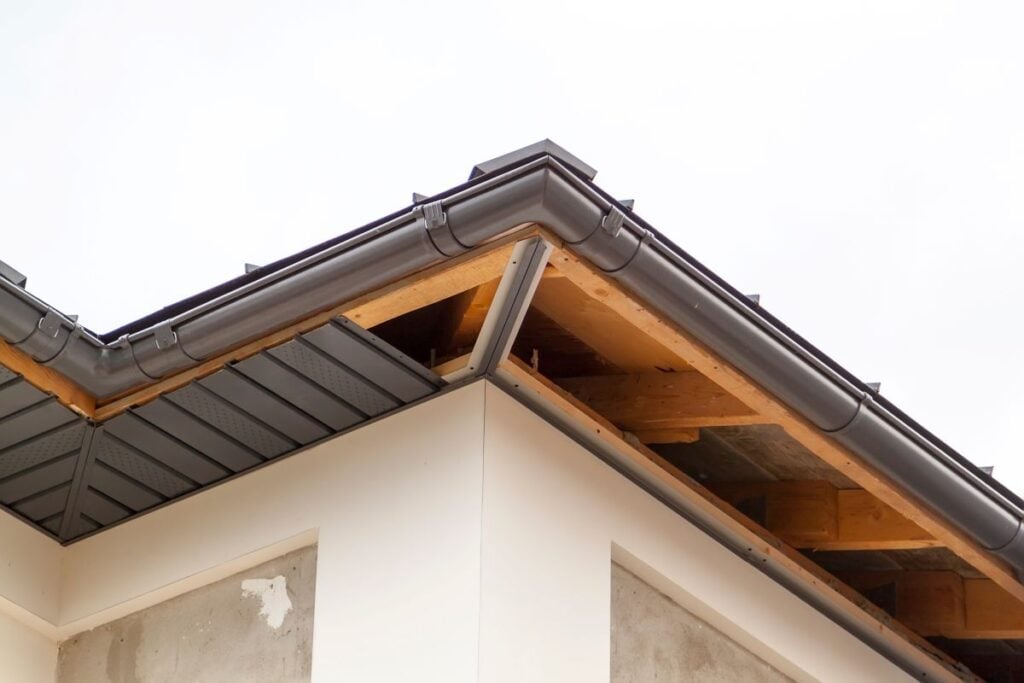 close-up view of corner of house with a gray roof and plums and filing of roof overhangs with soffits of house under construction
