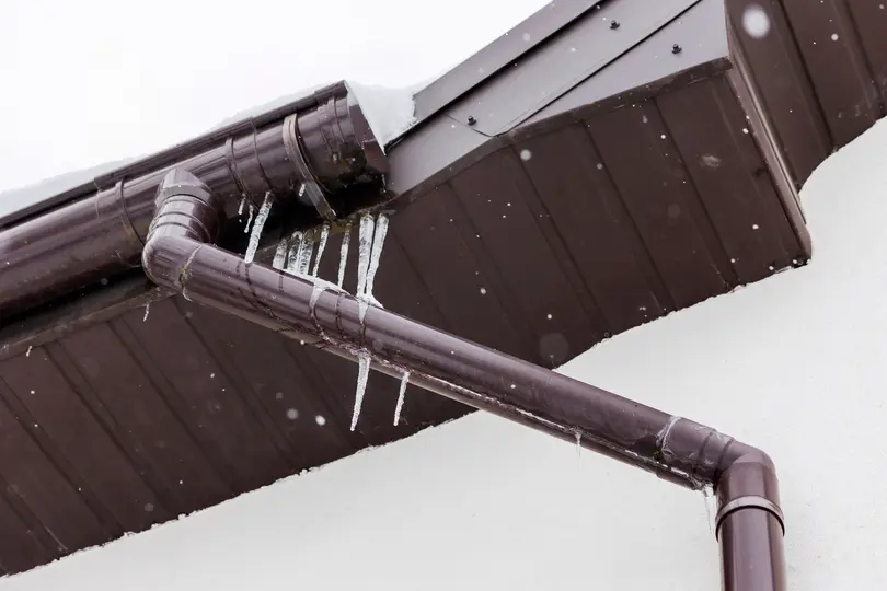 Frozen Ice on Roof Gutter in Winter, Ice Dam in Gutter of Roof House. Melting Snow Problems