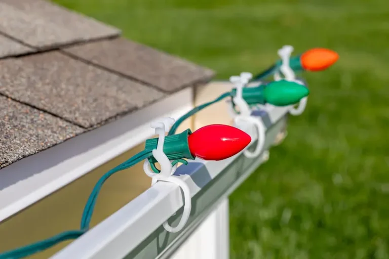 Hanging Christmas string lights on gutter of house. Holiday decorating safety, lighting and accident prevention concept